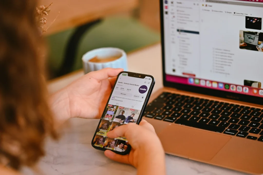 Persona Sosteniendo Un Smartphone Con Un Perfil De Redes Sociales Junto A Una Laptop