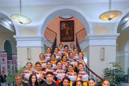 El equipo de capacitación de la Empresa Zulueta posa en primer plano, todos vestidos con camisetas negras con el logotipo de la firma. Detrás de ellos, en una elegante escalera, se encuentran las 17 embajadoras de la Feria Tabasco, vestidas con trajes regionales de blusa bordada con flores y falda.