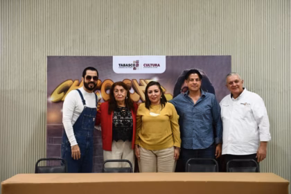 "Fotografía grupal durante la rueda de prensa del programa 'Chico Che por siempre'. Aparecen de izquierda a derecha: el artista Chico Che Chico vistiendo su icónico overol azul; Concepción Aurora Rodríguez Garduza (viuda de Chico Che); Aída Elba Castillo Santiago, Secretaria de Cultura de Tabasco; un colaborador de la dependencia y Salvador Manrique Priego, subsecretario de Desarrollo Cultural. Al fondo, un banner oficial con los logotipos del Gobierno de Tabasco y la Secretaría de Cultura."