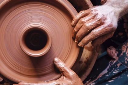 Una vista aérea picada (cenital) captura un primer plano extremo de las manos de un artesano alfarero cubiertas de barro arcilloso de color terracota.