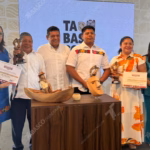 Fotografía Grupal Durante La Presentación Del Reconocimiento De Excelencia Artesanal 2026 En Tabasco. En El Centro, Los Artesanos Ganadores Sostienen Sus Reconocimientos Y Trofeos Junto A Autoridades Estatales. Al Frente, Sobre Una Mesa De Madera, Se Exhiben Piezas Artesanales: Una Canoa Tallada Con Un Pescador Y Una Máscara Tradicional De La Danza Del Pochó. El Fondo Muestra El Logotipo De &Quot;Tabasco&Quot; Y Un Patrón De Iconografía Regional.