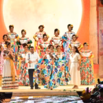 Fotografía De Plano General En Un Escenario De La Feria Tabasco. El Gobernador Del Estado Le Coloca Oficialmente La Banda Bordada De 'Embajadora' A Una Joven Que Representa Al Municipio De Centla, Quien Modela Sosteniendo La Amplia Falda Bordada En Flores De Su Traje Regional.