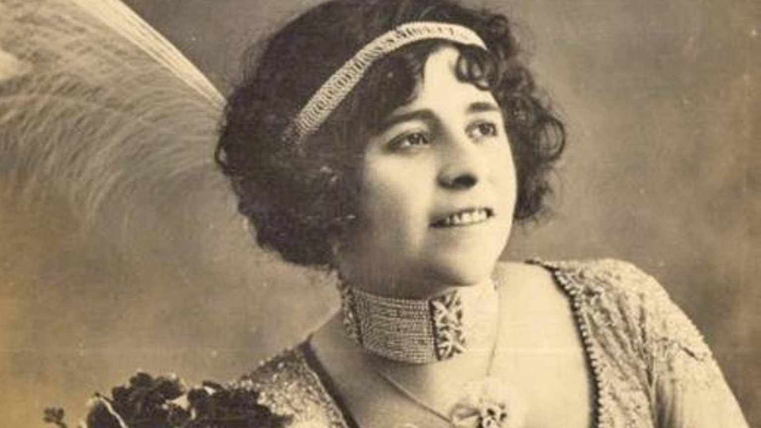 Legendaria Esperanza Iris En Villahermosa: Legado Cultural 2026 69 Retrato De Estudio En Sepia De Esperanza Iris, La Cantante Y Empresaria Teatral Tabasqueña. La Artista Aparece Sonriendo Levemente Y Mirando Hacia Arriba Y A La Derecha. Luce Un Peinado Alto Con Rizos Y Una Banda Para La Cabeza Enjoyada Con Un Colgante. Un Gran Plumaje Blanco Asoma Por Detrás De Su Cabeza A La Izquierda. Lleva Un Collar Tipo Gargantilla Ancho Y Enjoyado Y Un Vestido Con Lentejuelas. El Fondo Es Un Degradado Suave Y Desenfocado.