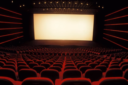 Una Fotografía En Gran Angular Que Muestra El Interior De Una Sala De Cine Vacía Con Una Atmósfera Cinematográfica Y Solemne. La Perspectiva Se Sitúa Desde Las Filas Traseras, Mirando Hacia Una Pantalla Blanca De Gran Formato Que Ilumina El Espacio.