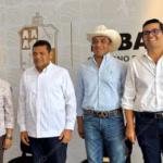 Cuatro Funcionarios Públicos De Tabasco Posan De Pie Frente A Un Muro Con El Logotipo Oficial Del Gobierno Del Estado. De Izquierda A Derecha: Una Mujer Con Camisa Floral, El Gobernador Javier May Rodríguez En Guayabera Blanca, Un Hombre Con Sombrero Vaquero Y Camisa Clara, Y Un Hombre Con Anteojos Y Camisa Blanca.