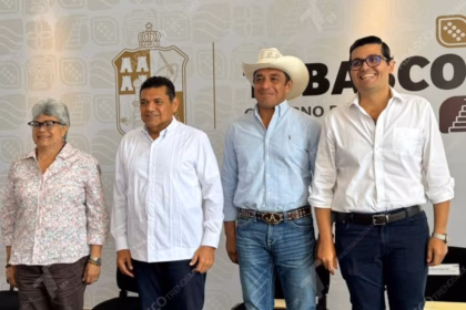 Cuatro Funcionarios Públicos De Tabasco Posan De Pie Frente A Un Muro Con El Logotipo Oficial Del Gobierno Del Estado. De Izquierda A Derecha: Una Mujer Con Camisa Floral, El Gobernador Javier May Rodríguez En Guayabera Blanca, Un Hombre Con Sombrero Vaquero Y Camisa Clara, Y Un Hombre Con Anteojos Y Camisa Blanca.