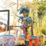 Mariú Mendoza Cabrera, Embajadora De Emiliano Zapata, Viste Un Traje De Gala Con Plumas Azul Turquesa Y Pedrería, Saludando Desde Un Carro Alegórico Decorado Con Flores De Lluvia De Oro Y Elementos Que Representan La Fauna Del Río Usumacinta.