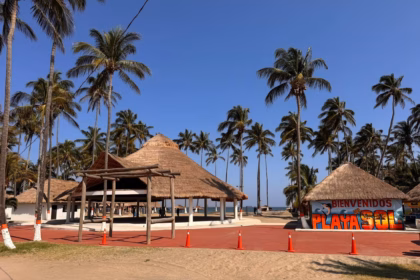 Fotografía Del Acceso Principal A Playa Del Sol En Paraíso, Tabasco, Bajo Un Cielo Azul Despejado. En Primer Plano Hay Un Camino De Arena Y Una Franja Pavimentada De Color Rojo Delineada Con Conos De Tráfico Naranjas Para Guiar El Flujo De Visitantes.