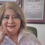 Una Fotografía De Plano Medio De Chely Caraveo P. (Nombre De Pila: Consuelo María Caraveo De Mendoza), Directora Del Instituto Sinde En Tabasco. Aparece Sentada En Una Oficina, Sonriendo Cálidamente A La Cámara Y Sosteniendo Su Barbilla Con La Mano Derecha. Viste Una Camisa Blanca Formal.