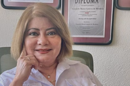 Una Fotografía De Plano Medio De Chely Caraveo P. (Nombre De Pila: Consuelo María Caraveo De Mendoza), Directora Del Instituto Sinde En Tabasco. Aparece Sentada En Una Oficina, Sonriendo Cálidamente A La Cámara Y Sosteniendo Su Barbilla Con La Mano Derecha. Viste Una Camisa Blanca Formal.