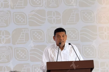 El Gobernador De Tabasco, Javier May Rodríguez, De Pie Tras Un Podio Con Micrófonos, Vistiendo Una Guayabera Blanca Tradicional.