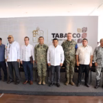 Una Fotografía De Cuerpo Entero Muestra A Un Grupo De Diez Hombres De Mediana Edad, Incluyendo Funcionarios Del Gobierno En Guayaberas Y Militares En Uniforme, Posando De Pie En Una Tarima En Una Sala De Conferencias Moderna. Están Frente A Un Telón De Fondo De Marca Que Muestra El Escudo De Armas De Tabasco Y El Texto Que Dice &Quot;Tabasco Gobierno Del Pueblo&Quot;.