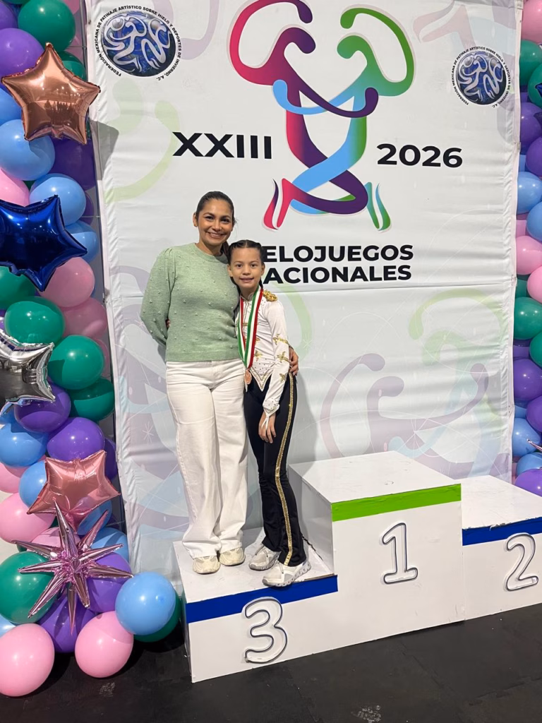 Una Fotografía Vertical De La Joven Patinadora Artística Tabasqueña, Mariana Rovirosa Priego, Posando Con Una Sonrisa En El Tercer Escalón Del Podio De Premiación Junto A Su Entrenadora, La Coach Rocío Rodríguez.