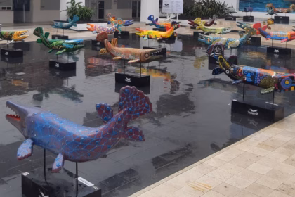 Una Fotografía Panorámica Del Patio Central De La Plaza “La Ceiba” En El Palacio Municipal Del Centro, Villahermosa. En Primer Plano Y Extendiéndose Hacia El Fondo, Sobre Un Espejo De Agua Reflectante Que Cubre El Suelo, Se Observan Decenas De Esculturas Monumentales De Pejelagartos De Fibra De Vidrio.