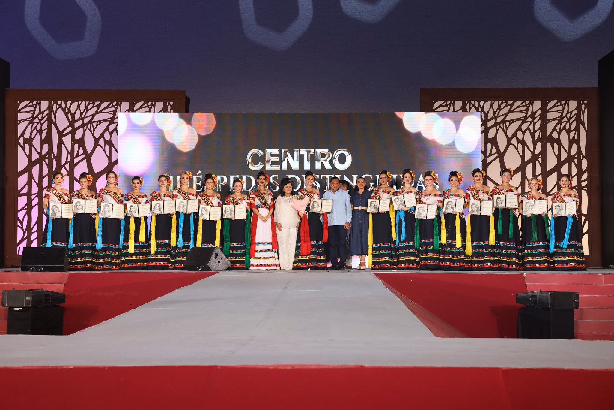 El Gobernador Javier May Rodríguez Y La Alcaldesa Yolanda Osuna Huerta Posan En El Escenario De La Plaza De La Revolución Junto A Las 17 Embajadoras De La Feria Tabasco 2026, Quienes Sostienen Sus Reconocimientos De Huéspedes Distinguidas Vistiendo El Traje Regional Tabasqueño.