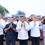Fotografía A Nivel De Ojo Y Formato Horizontal Que Muestra Al Gobernador De Tabasco, Javier May Rodríguez, Al Centro De Una Línea De Funcionarios Públicos Y Ciudadanos De Pie. El Mandatario Viste Una Guayabera Blanca Con Detalles Bordados Verticales Al Frente Y Sonríe Mientras Aplaude.