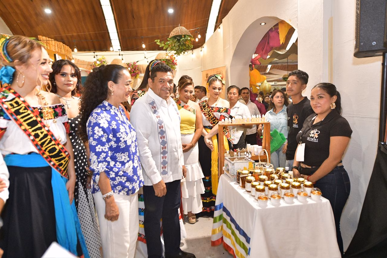 Apicultores Y Cacaoteros Destacan Impulso Al Campo En Los Pabellones De Emiliano Zapata Y Cunduacán 70 Fotografía A Color Tomada Desde Un Ángulo Bajo, Que Captura Un Recorrido Oficial Por Un Stand De Feria. En El Centro, El Gobernador Javier May Rodríguez, Vestido Con Una Guayabera Blanca Bordada, Sonríe A La Cámara. A Su Lado, Aurora Raleigh De La Cruz Viste Una Camisa Azul Con Flores Blancas.