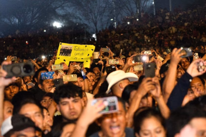 Una Multitud De Personas Disfruta De Un Concierto Nocturno En La Feria Tabasco 2026. Los Asistentes Levantan Sus Teléfonos Celulares Para Grabar El Espectáculo, Creando Puntos De Luz Entre La Audiencia. En El Centro, Destaca Un Fan Que Sostiene Una Cartulina Amarilla Fluorescente Con La Frase &Quot;Tabasco Ama A...&Quot; Y Una Fotografía Del Grupo Musical. El Ambiente Es De Celebración Y Entusiasmo Colectivo.