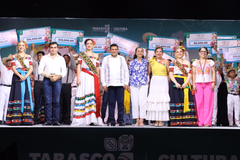 Fotografía Grupal Sobre Un Escenario Iluminado Durante La Feria Tabasco. En El Centro Destaca El Gobernador Javier May Rodríguez Con Guayabera Blanca, Acompañado Por Aurora Raleigh De La Cruz (Camisa Azul Floral) Y La Flor Tabasco 2026, María José Hernández Vera, En Traje Regional Blanco. A Los Costados Se Encuentran Las Embajadoras De Emiliano Zapata Y Cunduacán, Junto A Autoridades Municipales.
