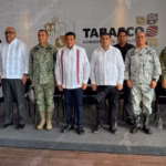 Otografía De Prensa En Plano Entero Y Ángulo Frontal Que Muestra A Diez Funcionarios Públicos Alineados De Pie Sobre Un Presídium Durante Una Conferencia De Prensa Del Gobierno De Tabasco. Al Centro Destaca El Gobernador Javier May Rodríguez Vistiendo Una Guayabera Blanca Con Bordados Verticales Rojos Y Pantalón Oscuro.