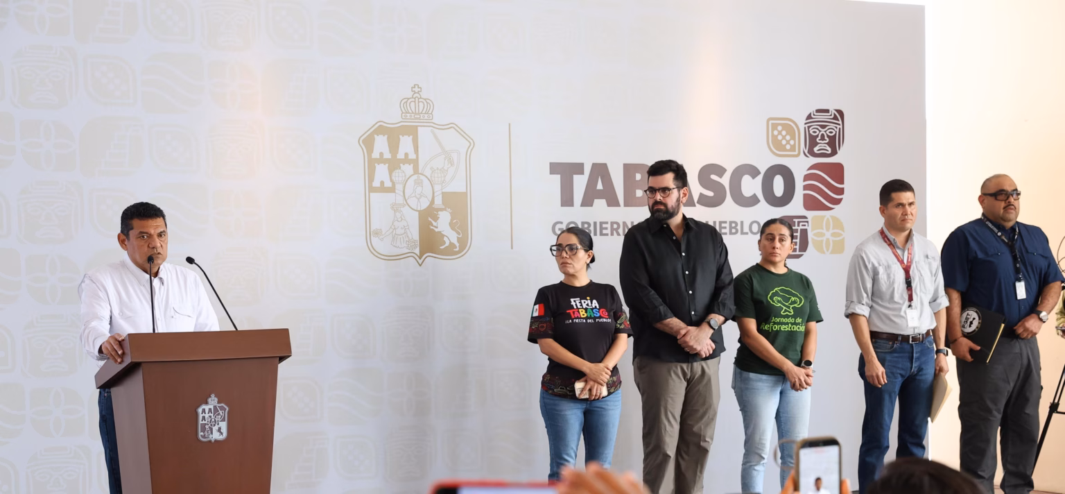 El Gobernador Javier May Rodríguez En El Podio Durante Una Conferencia De Prensa, Acompañado Por Miembros De Su Gabinete Y Equipo De Trabajo, Quienes Permanecen De Pie A Su Lado Frente A Un Muro Con El Logotipo Oficial Del Gobierno De Tabasco.