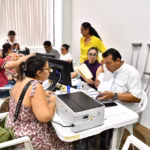 Fotografía En Plano Medio De Una Mesa De Atención Administrativa Donde Personal Del Gobierno Del Estado Revisa Documentos De Ciudadanos. En Primer Plano, Un Hombre Con Camisa Blanca De Manga Corta Y Una Mujer Con Blusa Morada Analizan Expedientes En Papel Y Consultan Una Computadora De Escritorio.