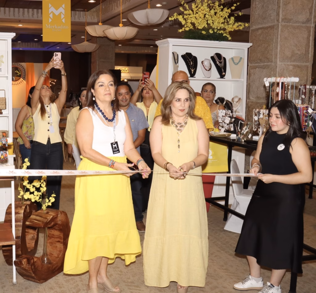 Las Organizadoras De Merkadito Bazar, Claudia Vargas Berman Y Cristel Dueñas Zurita, Realizan El Corte De Listón Inaugural De La 10ª Edición En El Hotel Hyatt Regency Villahermosa. Ambas Visten Atuendos En Color Amarillo Y Blanco, Sosteniendo Las Tijeras Mientras Se Preparan Para Abrir Oficialmente El Evento.