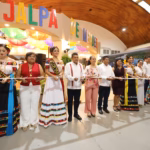Fotografía De Una Ceremonia De Corte De Listón Frente A La Entrada Del Pabellón De Jalpa De Méndez. En El Centro, El Gobernador Javier May Rodríguez Sostiene Las Tijeras Junto A Aurora Raleigh De La Cruz (Blusa Rosa Floral) Y La Flor Tabasco 2026, María José Hernández Vera, En Traje Regional Blanco. A La Izquierda Destacan La Embajadora De Jonuta Con Su Banda Oficial Y Autoridades Municipales Con Chalecos Rojos Y Blancos.