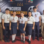 Otografía Horizontal En Plano General Que Captura La Ceremonia De Inauguración Del Concurso Cinematográfico Académico En Un Auditorio. En La Parte Izquierda, Un Hombre Con Camisa Blanca De Manga Larga Y Pantalón Caqui Permanece De Pie Junto A Un Grupo De Cinco Estudiantes (Tres Mujeres Y Dos Hombres) Alineados Al Centro; Todos Los Alumnos Visten El Uniforme Institucional Conformado Por Camisas Polo Blancas Con Cuellos Oscuros, Pantalones O Faldas Oscuras Y Zapatos Negros.