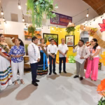 El Gobernador Javier May Rodríguez Junto A La Presidenta Honoraria Del Dif Tabasco, Aurora Raleigh De La Cruz, Y La Flor De Oro, María José Hernández Vera, Recorren El Stand De Emiliano Zapata En La Feria Tabasco 2026. En El Interior Del Espacio, Decorado Con Cuadros Artísticos, Plantas Colgantes Y Una Serie De Luces Cálidas, Un Expositor Explica Los Detalles De La Muestra Cultural A Las Autoridades Y A La Embajadora Del Municipio, Mariú Mendoza Cabrera. A La Derecha Destaca Un Retrato Enmarcado Sobre Una Estructura De Bambú Adornada Con Flores Multicolores De Gran Tamaño.