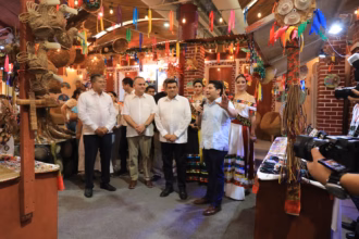 Fotografía Del Gobernador Javier May Rodríguez, Acompañado Por La Flor Tabasco 2026 Y Alcaldes, Durante El Recorrido Por Los Pabellones Municipales En La Nave 2 &Quot;Macuilís&Quot;. El Grupo Se Encuentra Frente A Un Stand Decorado Con Artesanías De Mutusay Y Fibras Naturales, Mientras Un Edil Explica Las Muestras Culturales.