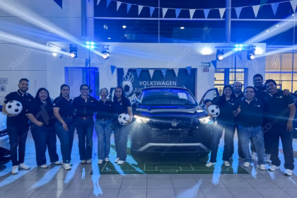Una Fotografía De Ángulo Medio Captura A Un Grupo Grande De Doce Empleados, De Diversas Edades Y Géneros, Posando Con Entusiasmo En Un Concesionario De Volkswagen Para El Lanzamiento De Una Edición Limitada. Visten Camisetas De Uniforme Negras Con Logos De Volkswagen Y Goal 2026.