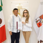 Fotografía De Plano Medio En Formato Horizontal Que Muestra Al Gobernador De Tabasco, Javier May Rodríguez, Y A La Arquitecta Alejandra Cámara Martínez Posando De Frente En Una Oficina Institucional. A La Izquierda, El Gobernador Viste Una Guayabera Blanca De Manga Larga Con Alforzas Y Bordados Azules Verticales, Combinada Con Pantalón Oscuro. A La Derecha, Alejandra Cámara