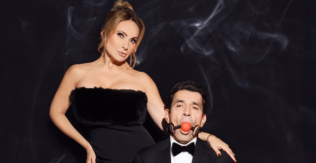 El Juego Del Deseo Y El Poder Llega A Villahermosa: Jorge Salinas Y Elizabeth Álvarez Encabezan “La Obscenidad De La Carne” 70 Retrato Promocional De Los Actores Elizabeth Álvarez Y Jorge Salinas Sobre Un Fondo Negro Con Sutiles Ráfagas De Humo Blanco. A La Izquierda, La Actriz Posa De Pie Con Un Vestido Negro Strapless Texturizado, Pendientes Largos Y El Cabello Recogido, Mirando Fijamente A La Cámara Con Una Expresión De Poder. A La Derecha, En Primer Plano, El Actor Viste Un Esmoquin Negro Con Pajarita Y Aparece Amordazado Con Una Mordaza De Bola Roja Sujeta Por Correas De Cuero Negras, Mientras La Mano De La Actriz Reposa Sobre Su Hombro.