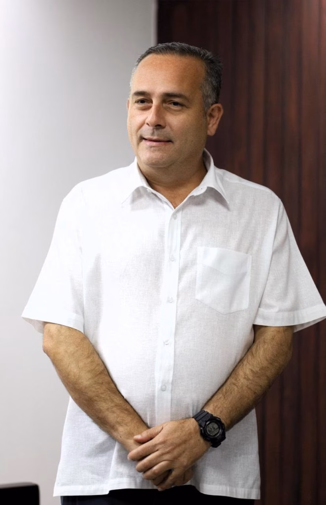 Resultados Tangibles En Tabasco: Más De 5 Mil Vinculaciones A Proceso Y 1,600 Sentencias Consolidan El Poder Judicial 71 Retrato Institucional De Medio Cuerpo Del Magistrado Carlos Efraín Reséndez Bocanegra, Presidente Del Tribunal Superior De Justicia De Tabasco. El Funcionario Aparece De Pie, Vistiendo Una Guayabera Blanca Formal De Manga Corta Con Las Manos Entrelazadas Al Frente. El Fondo Combina Una Pared Clara Y Un Panel De Madera Oscura Vertical, Con Una Iluminación De Estudio Profesional.