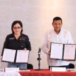 Fotografía De Prensa En Interiores Que Muestra A La Coordinadora Nacional De Protección Civil, Laura Velázquez Alzúa, Y Al Gobernador De Tabasco, Javier May Rodríguez, De Pie Detrás De Una Mesa Con Mantel Rojo. Ambos Sostienen Carpetas Abiertas Mostrando Documentos Oficiales Firmados, En El Evento Capturado En &Quot;Javier May Coordina Plan De Emergencia Por Temporada De Lluvias En Tabasco