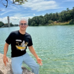 Io Camejo, Sonriente Y Con Gafas De Sol, Sentado Sobre Un Muro De Piedra A Orillas De La Laguna De Las Ilusiones En Villahermosa, Vistiendo La Misma Playera Negra De La Habana.