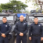 Tres Elementos Masculinos De La Secretaría De Seguridad Y Protección Ciudadana De Tabasco Posan De Pie Y De Frente En Plano Medio, Vistiendo Uniformes Policiales Oficiales De Color Azul Marino Con Insignias Y Placas En El Pecho. Detrás De Ellos Se Encuentran Estacionadas Dos Patrullas Blindadas Tácticas De Color Negro Tipo &Quot;Black Mamba&Quot; Con Luces De Torreta En El Techo Y Placas De Circulación Del Estado De Tabasco Visibles Al Frente. De Fondo Se Aprecian Árboles Verdes Bajo Un Cielo Claro.