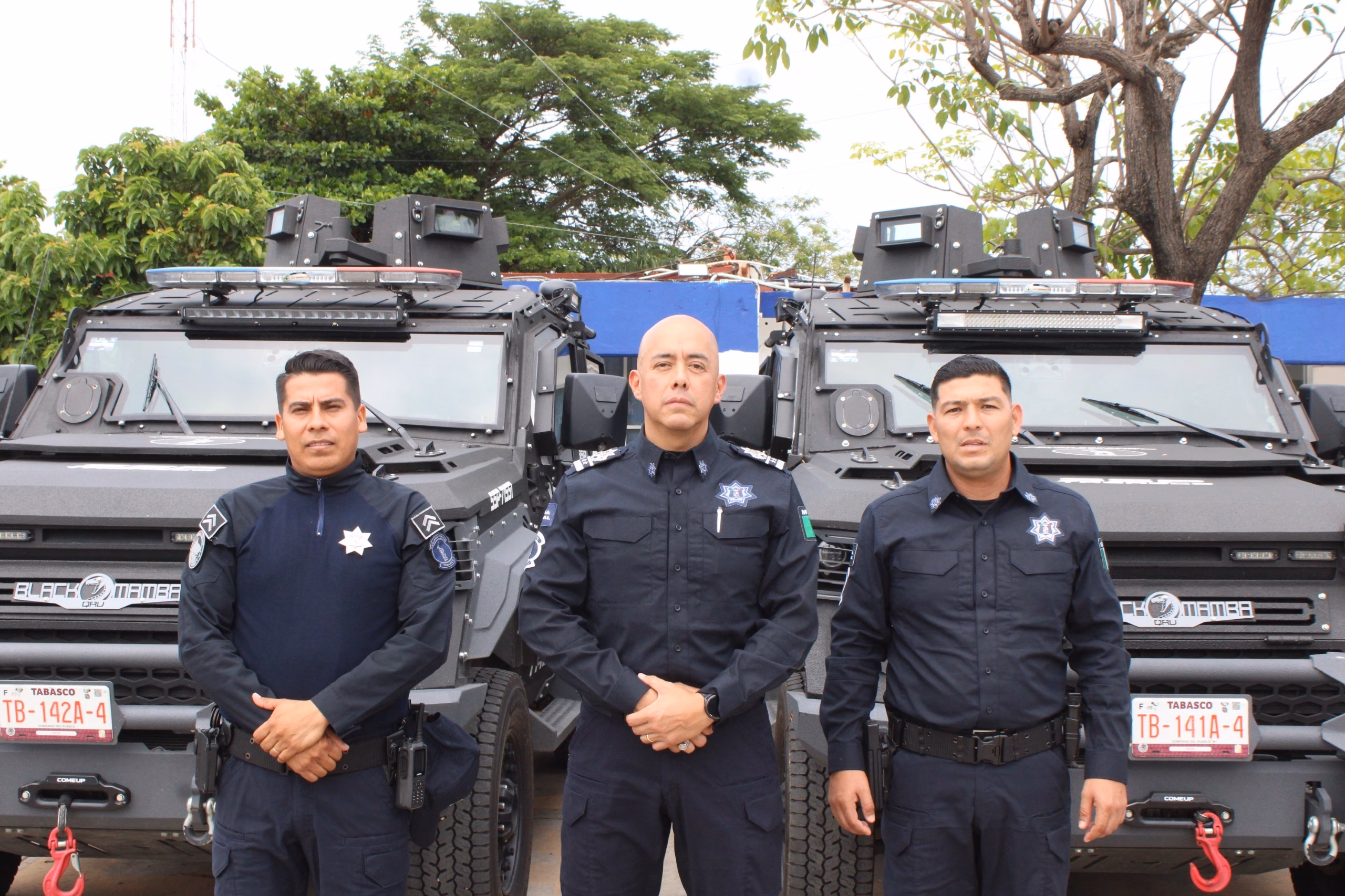 Refuerzan La Seguridad En Tabasco: Realiza Sspc Nuevos Nombramientos En Direcciones Operativas 2 Tres Elementos Masculinos De La Secretaría De Seguridad Y Protección Ciudadana De Tabasco Posan De Pie Y De Frente En Plano Medio, Vistiendo Uniformes Policiales Oficiales De Color Azul Marino Con Insignias Y Placas En El Pecho. Detrás De Ellos Se Encuentran Estacionadas Dos Patrullas Blindadas Tácticas De Color Negro Tipo &Amp;Quot;Black Mamba&Amp;Quot; Con Luces De Torreta En El Techo Y Placas De Circulación Del Estado De Tabasco Visibles Al Frente. De Fondo Se Aprecian Árboles Verdes Bajo Un Cielo Claro.