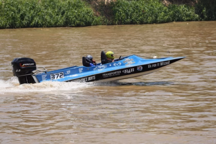 Una Lancha De Carreras Azul Con El Número 372 Y Un Motor Fuera De Borda Mercury Navega A Gran Velocidad Sobre El Agua Color Café Del Río Grijalva. Dos Tripulantes Con Cascos De Protección Van A Bordo Mientras La Embarcación Deja Una Estela De Agua Tras De Sí, Con Vegetación Verde Visible Al Fondo En La Orilla Del Río.