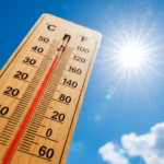 Termómetro De Madera En Primer Plano Apuntando Hacia El Cielo Azul Intenso Con El Sol Brillante Y Destellos De Luz. La Columna Roja Del Termómetro Marca Una Temperatura Alta Cercana A Los 50°C, Ilustrando Las Extremas Temperaturas Durante La Canícula 2026.