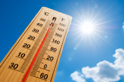 Termómetro De Madera En Primer Plano Apuntando Hacia El Cielo Azul Intenso Con El Sol Brillante Y Destellos De Luz. La Columna Roja Del Termómetro Marca Una Temperatura Alta Cercana A Los 50°C, Ilustrando Las Extremas Temperaturas Durante La Canícula 2026.