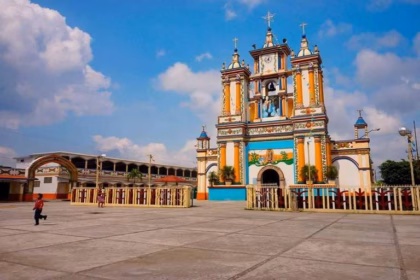 Fachada Colorida E Icónica De La Iglesia De La Virgen De La Asunción En Cupilco, Comalcalco, Pintada En Tonos Vivos De Amarillo, Azul, Verde Y Blanco, Con Una Amplia Plaza Frontal Bajo Un Cielo Despejado.