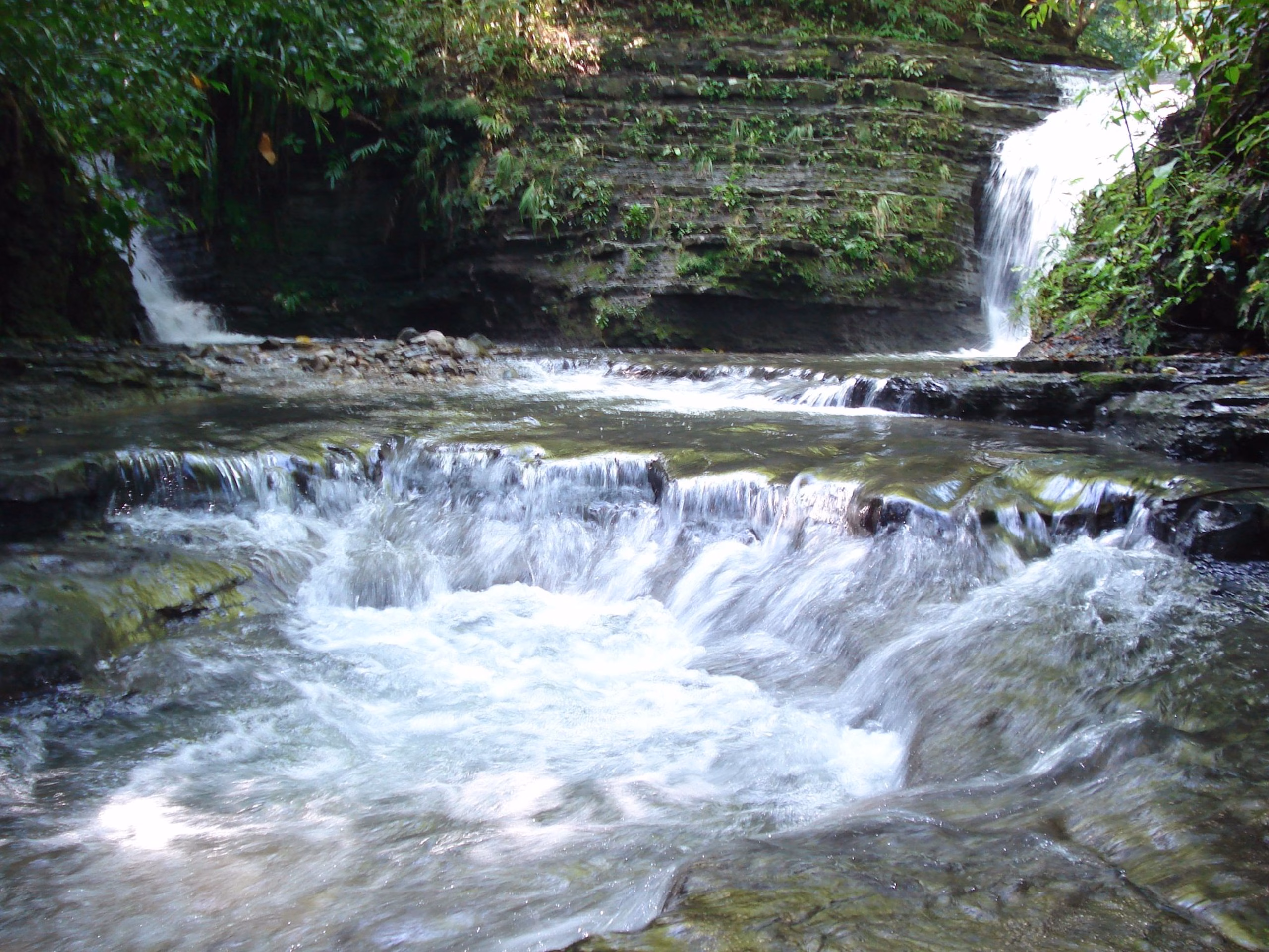 Una Cascada De Agua Cristalina Fluye Entre Rocas Escalonadas Formando Pequeñas Pozas Naturales En Medio De La Densa Selva De Huimanguillo. Al Fondo Se Aprecian Caídas De Agua Adicionales Y Paredes Rocosas Rodeadas De Vegetación Verde Y Húmeda.