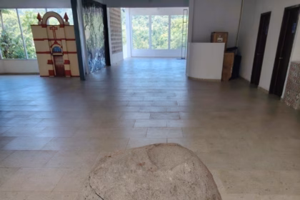 Una Gran Roca Esférica De Piedra Caliza, Con Una Fisura Diagonal, Exhibida En El Centro De Una Sala De Museo Sobre Un Piso De Losas Claras. Al Fondo, A La Izquierda, Se Observa Una Maqueta De La Fachada De Una Iglesia, Y A La Derecha, Una Ventana Que Da Al Exterior Y Puertas De Madera.
