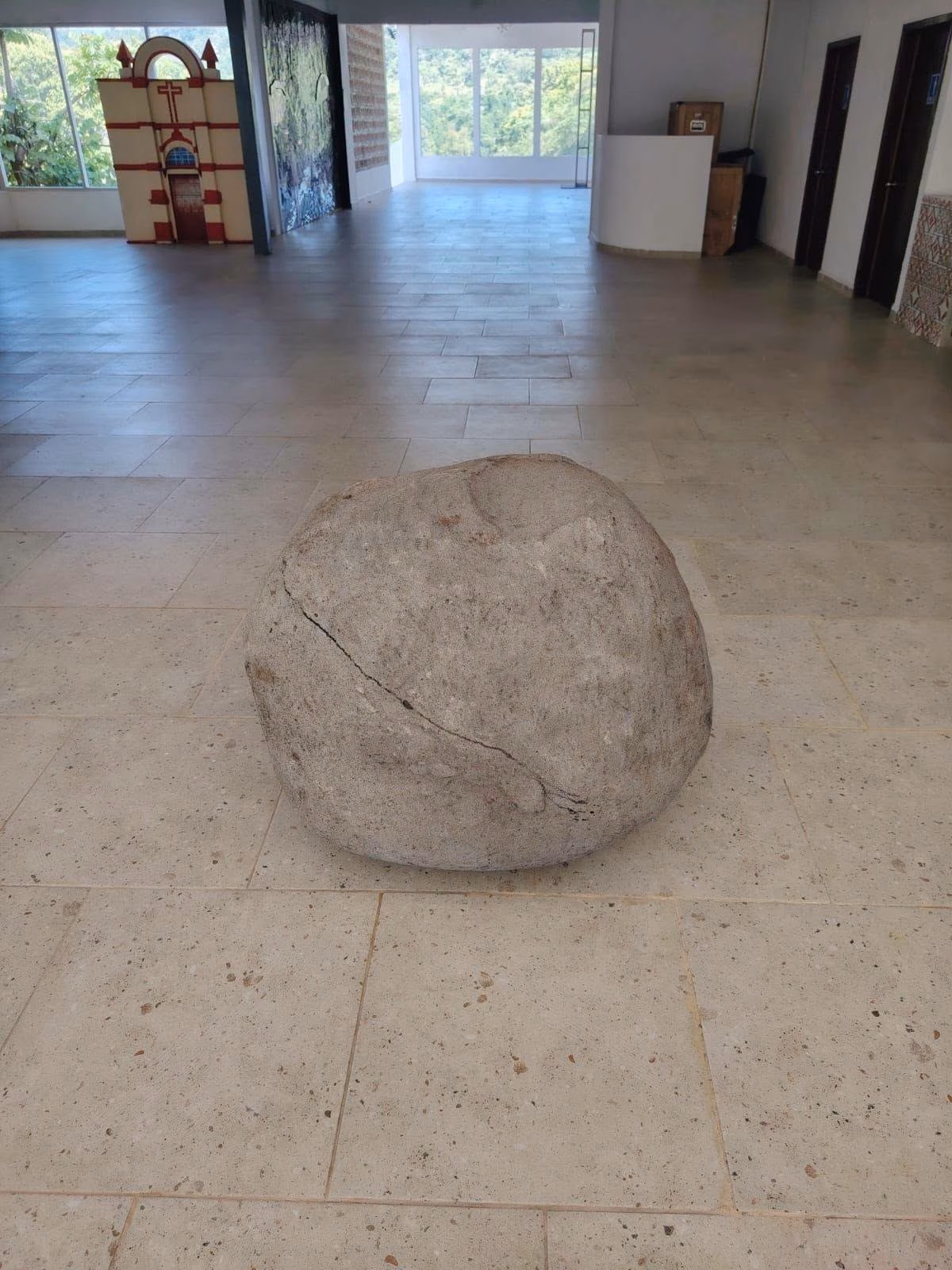 ¡El Misterio Milenario Al Descubierto: Hallan Impactante Petroglifo Prehispánico En Teapa 70 Una Gran Roca Esférica De Piedra Caliza, Con Una Fisura Diagonal, Exhibida En El Centro De Una Sala De Museo Sobre Un Piso De Losas Claras. Al Fondo, A La Izquierda, Se Observa Una Maqueta De La Fachada De Una Iglesia, Y A La Derecha, Una Ventana Que Da Al Exterior Y Puertas De Madera.