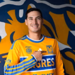 Mauro Lainez Sonriendo Mientras Señala El Escudo En El Pecho De La Camiseta Amarilla De Tigres De La Uanl.