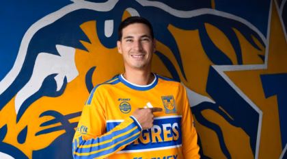 Mauro Lainez Sonriendo Mientras Señala El Escudo En El Pecho De La Camiseta Amarilla De Tigres De La Uanl.