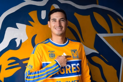 Mauro Lainez Sonriendo Mientras Señala El Escudo En El Pecho De La Camiseta Amarilla De Tigres De La Uanl.