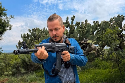 El Actor Tabasqueño Oswaldo Álvarez Caracterizado Con Ropa Casual Y Sosteniendo Un Arma Larga En Un Entorno De Campo Con Nopales, Durante Su Participación En Una Producción Dramática.